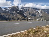 a motorcycle driving on a road between two mountains with a snow covered mountain in the distance