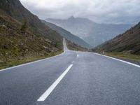 an empty highway running up the side of a mountain slope under stormy skies and clouds