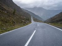 an empty highway running up the side of a mountain slope under stormy skies and clouds