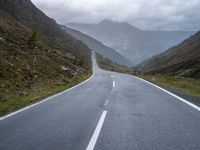 an empty highway running up the side of a mountain slope under stormy skies and clouds