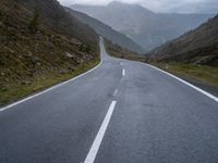 an empty highway running up the side of a mountain slope under stormy skies and clouds