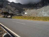 the mountains are towering above a lone highway, with a snow covered hill below it