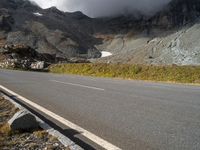 the mountains are towering above a lone highway, with a snow covered hill below it