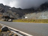 the mountains are towering above a lone highway, with a snow covered hill below it