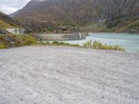 a small motorcycle is parked on a gravel road near the water and mountains on a cloudy day