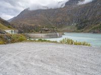 a small motorcycle is parked on a gravel road near the water and mountains on a cloudy day