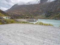 a small motorcycle is parked on a gravel road near the water and mountains on a cloudy day