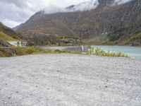 a small motorcycle is parked on a gravel road near the water and mountains on a cloudy day