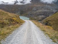 there is a dirt road running along the mountains with clouds and water in the sky