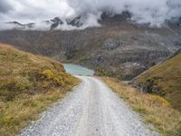 there is a dirt road running along the mountains with clouds and water in the sky