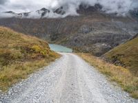 there is a dirt road running along the mountains with clouds and water in the sky