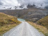 there is a dirt road running along the mountains with clouds and water in the sky