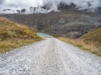 there is a dirt road running along the mountains with clouds and water in the sky