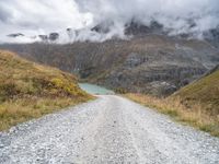 there is a dirt road running along the mountains with clouds and water in the sky