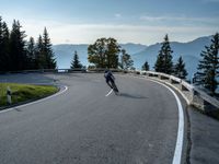 man riding on the road on his skateboard on a mountain side overlooking a lake