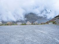 the motorcycle is sitting in a gravel lot on a mountain side with mist in the sky above