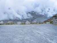 the motorcycle is sitting in a gravel lot on a mountain side with mist in the sky above