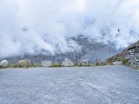 the motorcycle is sitting in a gravel lot on a mountain side with mist in the sky above