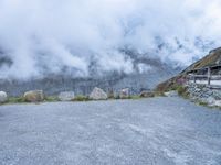 the motorcycle is sitting in a gravel lot on a mountain side with mist in the sky above