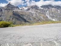 a red motorcycle is sitting on the road beside some mountains and trees, with snow capped peaks in the background
