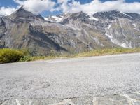 a red motorcycle is sitting on the road beside some mountains and trees, with snow capped peaks in the background