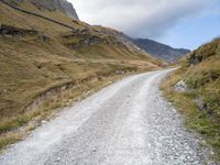 gravel road near a mountain with the sky in the background, with an orange and white bicycle in the foreground