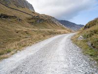 gravel road near a mountain with the sky in the background, with an orange and white bicycle in the foreground