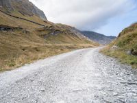 gravel road near a mountain with the sky in the background, with an orange and white bicycle in the foreground