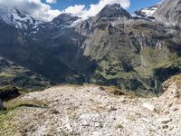 a person is standing near a mountain and looking at a valley below them with a dog, a cow and other animals