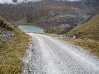 the gravel road leads to a water way in the mountains on a cloudy day with clouds