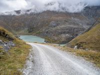 the gravel road leads to a water way in the mountains on a cloudy day with clouds