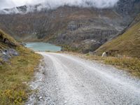 the gravel road leads to a water way in the mountains on a cloudy day with clouds