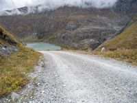 the gravel road leads to a water way in the mountains on a cloudy day with clouds