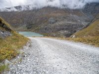 the gravel road leads to a water way in the mountains on a cloudy day with clouds