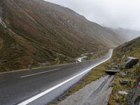 motorcycle parked in front of a mountainous hill on a cloudy day, with a small motorcycle parked beside the road