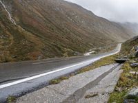 motorcycle parked in front of a mountainous hill on a cloudy day, with a small motorcycle parked beside the road