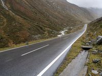 motorcycle parked in front of a mountainous hill on a cloudy day, with a small motorcycle parked beside the road