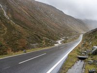 motorcycle parked in front of a mountainous hill on a cloudy day, with a small motorcycle parked beside the road