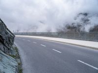 a road with rocks on either side and mountain in the background with mists over it