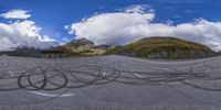 two mountains with some black circles on the road, and a bench in front of the mountain