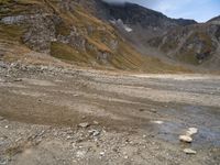 a dirt road with rocks and mountains in the background with water in between the rocks