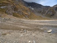 a dirt road with rocks and mountains in the background with water in between the rocks