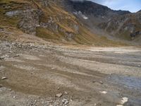 a dirt road with rocks and mountains in the background with water in between the rocks