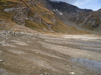 a dirt road with rocks and mountains in the background with water in between the rocks