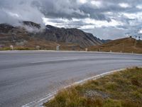 a mountain pass on a cloudy day with no cars on it, as the road winds through