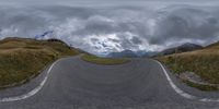 a curved curved road going past some mountains under cloudy skies overhead the image is taken at 360 angle