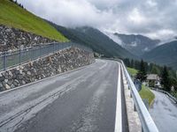 a paved mountain road passing through the countryside near mountains, with clouds on a hillside