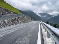 a paved mountain road passing through the countryside near mountains, with clouds on a hillside