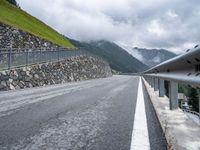 a paved mountain road passing through the countryside near mountains, with clouds on a hillside