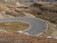 a curve in the mountain road, with two motorcycles on the side of it and mountains and fields in the background